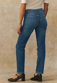Blå denim jeans med rak bendesign, hög midja, bakfickor och fållade kanter, kombinerade med svarta klackskor.