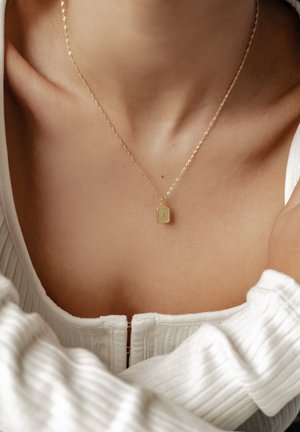 Goldpendant-Halskette an einer feinen Kette, mit einem rechteckigen Anhänger mit strukturierter Oberfläche, präsentiert auf einem hellen Oberteil.