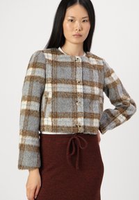 Grijze en bruine geruite cropped jack met een zachte textuur, voorzien van grote knopen en lange mouwen. Gecombineerd met een bruine rok met trekkoord.