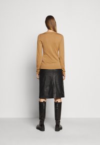 Hnědý pletený top s dlouhým rukávem v kombinaci s černou koženou midi sukní a lesklými černými kozačkami po kolena, pohled zezadu.