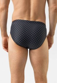 Donkere zwembroek met een patroon van kleine cirkels in rood en blauw. De stof lijkt glad met minimale rek en bedekking.