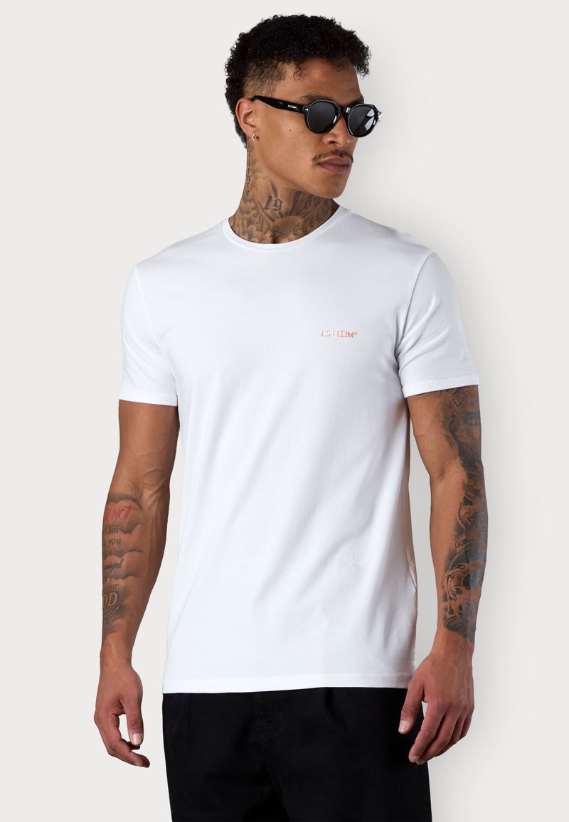 Weißes Kurzarm-T-Shirt aus Baumwolle mit Rundhalsausschnitt und einem kleinen roten Logo. Glatte Textur, taillierte Passform, kombiniert mit Sonnenbrille.