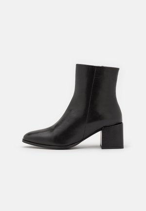 Svarte lærankelstøvler med firkantet tå og blokkhel. Glatt tekstur, minimalistisk design og sømløs konstruksjon.