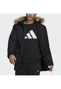 Černá puffer bunda s kapucí podloženou kožešinou, s bočními kapsami a předním zipem. Vnitřní podšívka je hladká, což kontrastuje s vnějším povrchem.