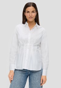 Camisa blanca de manga larga con botones, con un cuerpo ajustado y diseño peplum, combinada con unos vaqueros de mezclilla azul claro. Textura suave, cuello clásico.