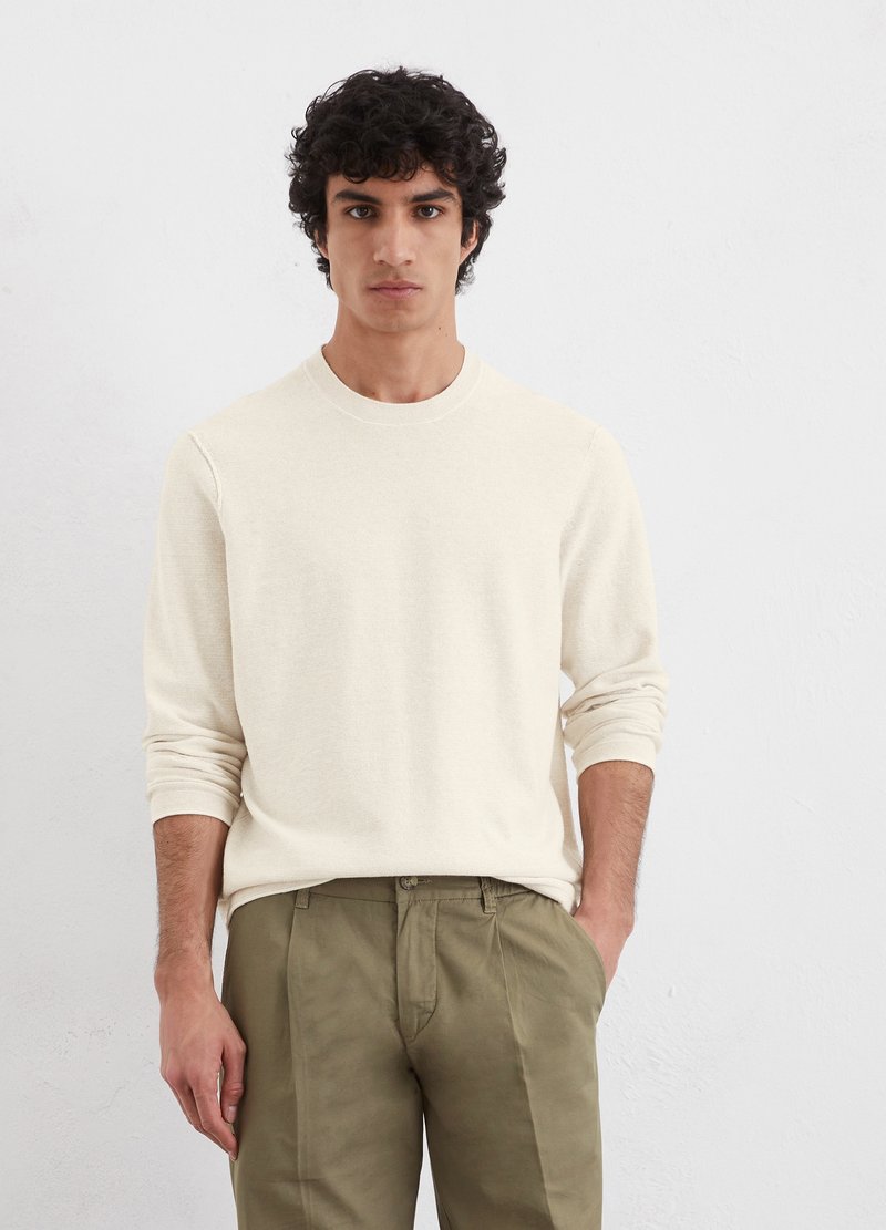Crème lange mouwen sweater, reguliere pasvorm, ronde halslijn, zachte textuur. Gecombineerd met olijfgroene broek, staande tegen een neutrale achtergrond.