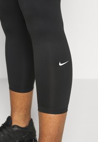 Black athletic leggings made of stretchy fabric, featuring a white Nike logo on the thigh and a close-fitting design.
