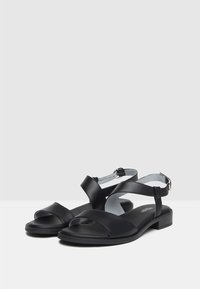 Sandali neri in pelle con fasce incrociate, design con punta aperta, cinturino regolabile alla caviglia con fibbia e tacco basso.