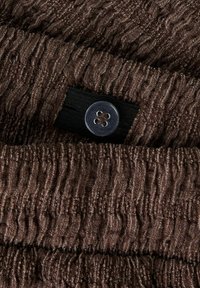 Tissu marron texturé avec des lignes verticales froissées, doté d'une bande élastique noire et d'un bouton argenté à quatre trous.