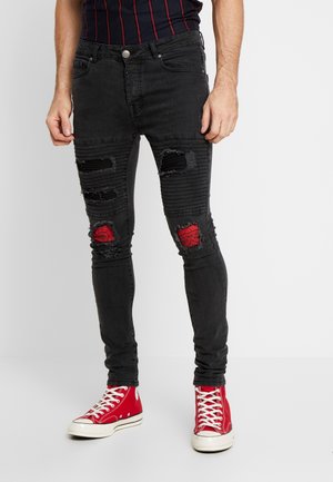 Mann trägt schwarze, abgenutzte Skinny-Jeans mit roten Flicken an den Knien und roten High-Top-Sneakers mit weißen Schnürsenkeln.