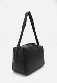 Borsa a duffel nera realizzata in materiale sintetico liscio. Presenta una forma rettangolare, una lunga tracolla regolabile e due manici corti.