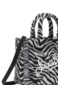 Sac rayé zèbre en tissu peluche noir et blanc, avec des accents à franges, double poignée supérieure et bandoulière amovible. Le texte à l'avant indique "Rêvant de Saint B."