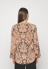 Langærmet bluse med paisley-mønster i fersken og sort. Har en rund halsudskæring og samlede mansjetter, samt et blødt, struktureret stof.