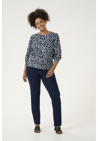 Zwart-wit gestreepte top met zebra-patroon in lichte stof, gestyled met driekwartmouwen, gecombineerd met donkerblauwe skinny jeans en zwarte hakken.