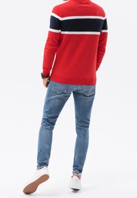 Rode trui met marineblauwe en witte horizontale strepen, gecombineerd met nauwsluitende blauwe spijkerbroek en witte sneakers. De trui heeft geribbelde manchetten en zoom.