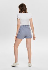 Stripete casual shorts med rynket midje, laget av lett stoff. Brukt med en tettsittende hvit t-skjorte og hvite joggesko.