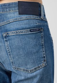 Blå denimjeans med en läderetikett som har "Marc O'Polo DENIM." Bakfickan har en liten etikett, med något blekning och kontrastsömmar.