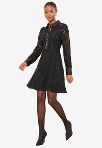 Mustast pitsist kleit pikkade varrukatega ja nööbitava esiosaga, millel on istuv korsett, lehviva seelik ning kontrastsed satiinist krae ja mansetid.