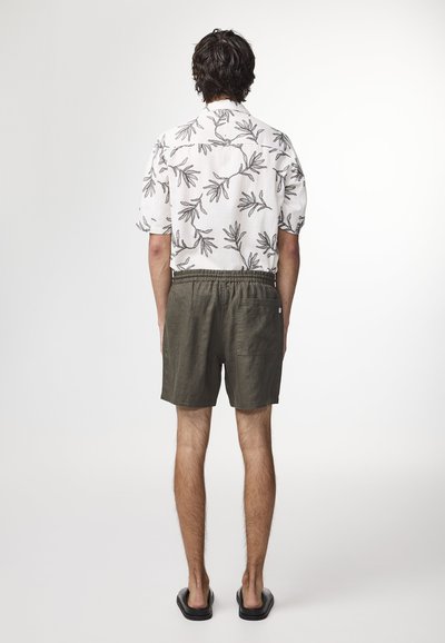 Camicia bianca a maniche corte con motivo a foglia nera, abbinata a pantaloni corti verde oliva con vita elastica e tasca posteriore.