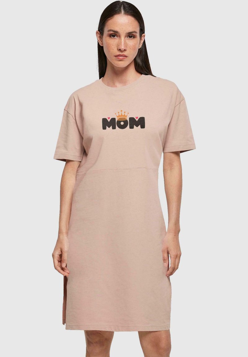 Světle růžové bavlněné šaty s volným střihem, vybavené krátkými rukávy a černou grafikou "MOM" se korunou a srdíčky. Postranní rozparky pro pohodlí.