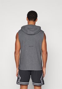 Felpa senza maniche grigia con orlo curvo e cappuccio, dotata di un logo discreto sul retro. Abbinata a pantaloni corti neri con accenti bianchi.