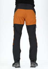 Herrernas vandringsbyxor med ett svart och orange färgblockdesign, tillverkade av flexibelt material, med dragkedjefickor och ankelremmar.