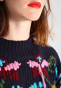 Pletený svetr v tmavě námořnické modři s žebrovaným límcem. Na přední straně barevné květinové vzory v růžové, červené, modré a zelené barvě. Texturovaná vlna.