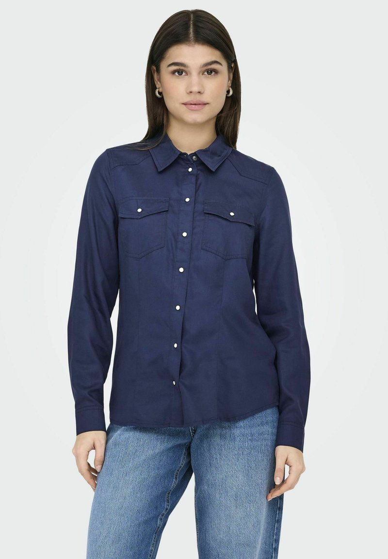 Camicia blu navy con colletto, dotata di due tasche sul petto e dettagli con bottoni argentati; realizzata in tessuto liscio, con maniche lunghe.