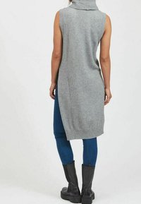 Ärmlös, grå, stickad turtleneck-klänning med sidospalter, ribbad fåll, matchad med blå jeans och svarta knähöga stövlar.