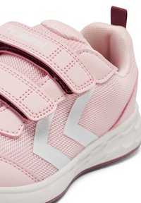 Baskets de sport roses en matériau mesh et synthétique, dotées de fermetures Velcro et d'accents blancs en zigzag. Design arrondi et semelle rembourrée.
