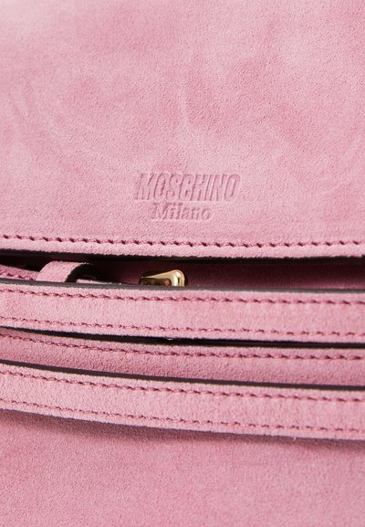 Rožā zamšādas rokassoma ar reljefa "Moschino Milano" logotipu, zelta metāla aksesuāriem un tonālā dūriena ap zipam.