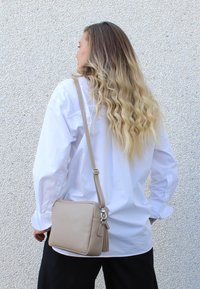 Borsa a tracolla in pelle beige con una finitura texturizzata, forma quadrata, tracolla regolabile e dettaglio con nappina.