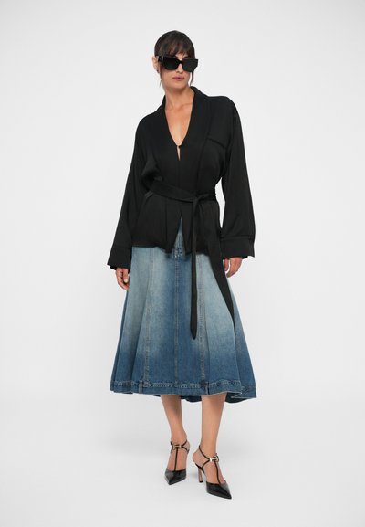 Black wrap-style blouse with long sleeves, paired with a denim skirt featuring an ombré effect. Accessories include black sunglasses and heeled shoes.