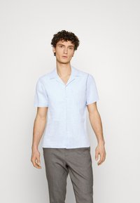 Light blue short-sleeve shirt made of linen, featuring a button-down front and notched collar. Worn with gray pants.