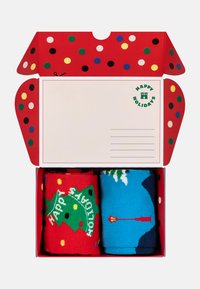 Red gift box with multi-colored dots, containing two pairs of socks: one with a Christmas tree design, the other in blue with a mountain scene.