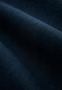 Tissu denim bleu foncé avec texture et tissage visibles, présenté en plis doux et en gros plan.