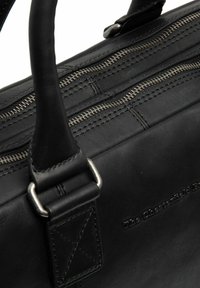 Bolso de cuero negro con dos compartimentos con cremallera, asas planas y costuras en contraste con una marca en relieve en el lateral.