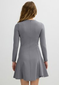 Vestido gris de manga larga con cuerpo ajustado y falda acampanada. Tejido suave con un brillo sutil, que cuenta con una cremallera en la parte posterior.