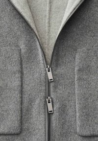 Grijze sweaterjack met een zachte binnenvoering, voorzien van twee voorzakken en dubbele ritsen. Gemaakt van textiel met een gladde afwerking.
