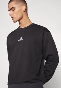 Sort sweatshirt lavet af bomuld med rund hals og lange ærmer. Har et lille gråt Adidas-logo på brystet.