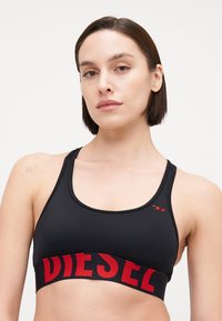Top sportivo nero con il logo rosso "DIESEL" sull'elastico, dotato di una texture liscia e spalline larghe, progettato per comfort e sostegno.
