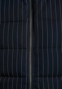 Chaleco acolchado azul marino con rayas blancas verticales, textura acolchada y cremallera metálica centrada para cierre.