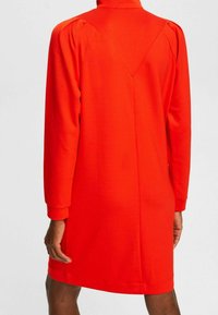 Czerwona sukienka bawełniana z długim rękawem, wysokim kołnierzem i subtelnym wzorem w kształcie litery V z tyłu. Posiada luźny krój i elastyczne mankiety.
