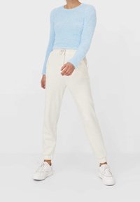Top de punto esponjoso de color azul claro de manga larga, combinado con joggers crema que tienen una cinturilla elástica y zapatillas blancas.