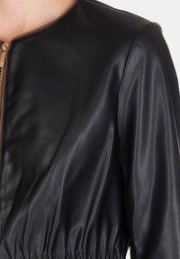 Giacca in pelle nera con scollo arrotondato, design aderente e dettagli arricciati in vita, con chiusura a zip.