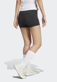 Pantaloni sportivi neri con cuciture a contrasto, aderenti. Indossati con calze bianche al ginocchio e sneakers di colore chiaro.