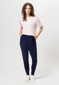 Camiseta rosa claro de manga corta combinada con pantalones elásticos de cintura navy que presentan un detalle de lazo, ambos complementados con zapatillas blancas.