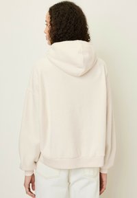 Hoodie oversize di un beige pallido, realizzato in morbido pile, con cappuccio, spalle scese e polsini e orlo a coste.