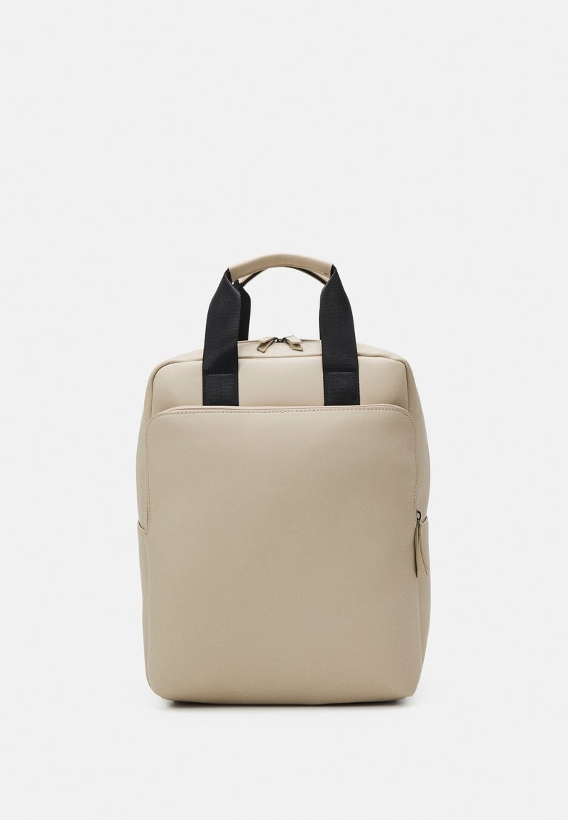 Sac rectangulaire beige avec poignées noires, une poche avant zippée et une fermeture éclair en haut sur un fond clair uni.