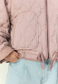 Quiltet rosa jakke med lynlås foran, to påsyede lommer og snoretræk detaljer i kanten, parret med lys denim.